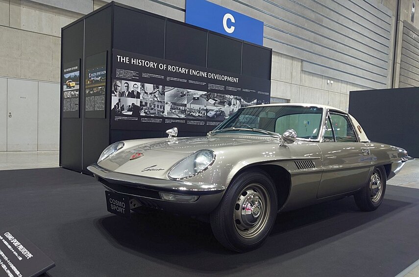А вот и сама Mazda Cosmo Sports: красивейшее двухместное купе с роторным двигателем объёмом 1 литр. Автомобиль это крайне редкий — с 1967 по 1972 год было выпущено всего 1176 машин двух серий. Но здесь перед нами редкость в квадрате: один из 47 предсерийных образцов, собранных в 1966 году и распределённых по дилерам для ознакомления. Причём эта машина, попавшая в префектуру Хёго, даже участвовала в гонках. Отличий от серийной версии немало, но заметит их только специалист: это чуть иные очертания переднего бампера без резиновых накладок, цельный задний бампер вместо составного, более крупная эмблема на передке, большие шильдики на задних стойках с изображением космических орбит вместо декоративных накладок, отсутствие «поворотников» за передними колёсами, один фонарь заднего хода вместо двух, отсутствие личинки замка багажника, иной рисунок отверстий в колёсных дисках, а внутри — другое расположение приборов.
