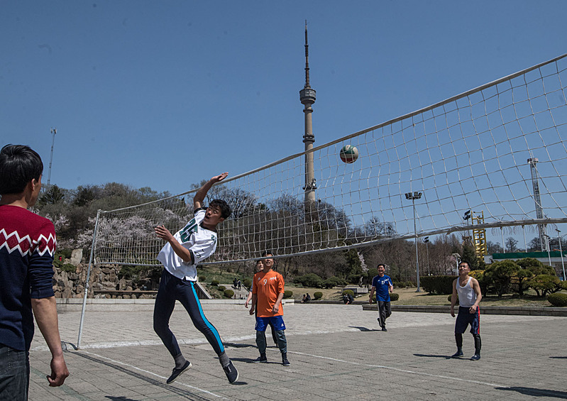 Молодые люди играют в волейбол возле Пхеньянской телебашни