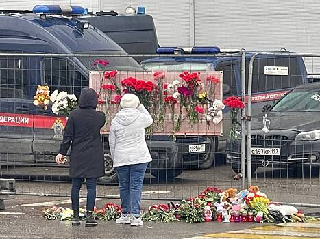 Люди возлагают цветы и крестятся у обломков здания Crocus City Hall, где накануне террористы расстреляли десятки людей