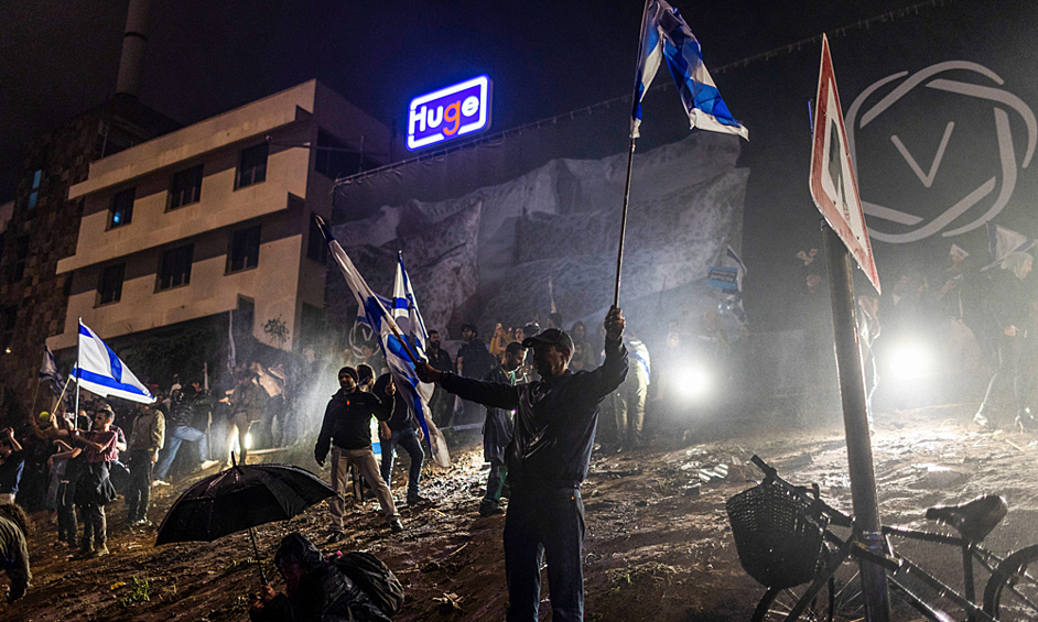 Протестующие держат израильские флаги во время столкновений с полицией на массовой антиправительственной акции протеста, 27 марта 2023 года