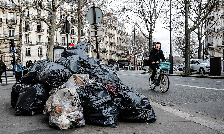 Мужчина проезжает мимо горы мусора на одной из улиц Парижа, 12 марта 2023 года