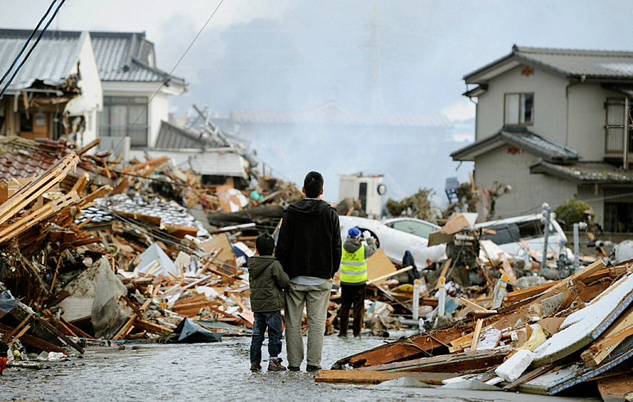 Отец с ребенком смотрят на разрушенный дом после землетрясения в Японии в 2011 году.