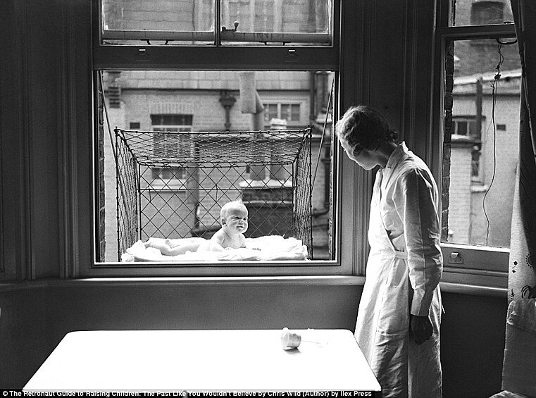 Младенец дышит свежим воздухом в клетке, вывешенной за окно.
