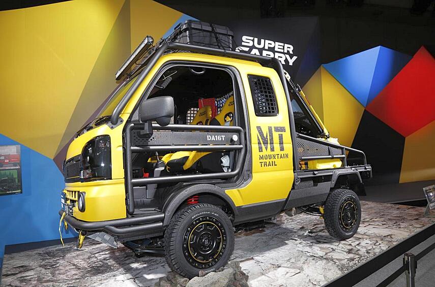 А тут у нас забавная имитация: микрогрузовичок Suzuki Super Carry будто бы подготовили для работы на тяжелых горных тропах. У него и каркас безопасности, и трубчатые «калитки», и здоровенные буксировочные проушины, и довольно зубастые шины, а сзади даже приторочен реечный домкрат-хайджек! Но всё это не должно обманывать: перед нами шоу-кар.