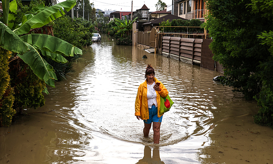 Женщина переходит улицу, затопленную в результате сильного ливня в поселке Мирный