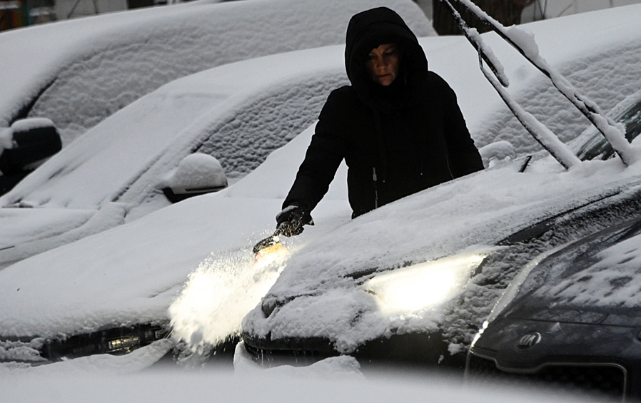 Женщина очищает машину от выпавшего снега в Москве, 16 ноября 2022 года
