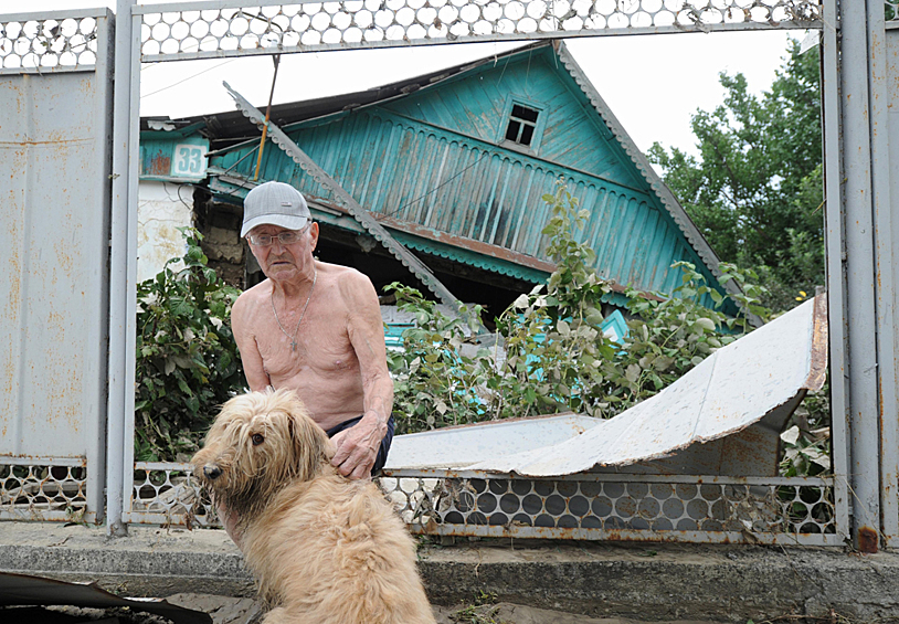 Пожилой мужчина с собакой у забора жилого дома, разрушенного наводнением в городе Крымск в Краснодарском крае