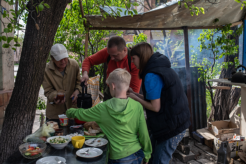 Ирина Григорьевна Чуприна с сыном Александром его супругой и детьми накрывают на стол во дворе жилого дома в Мариуполе