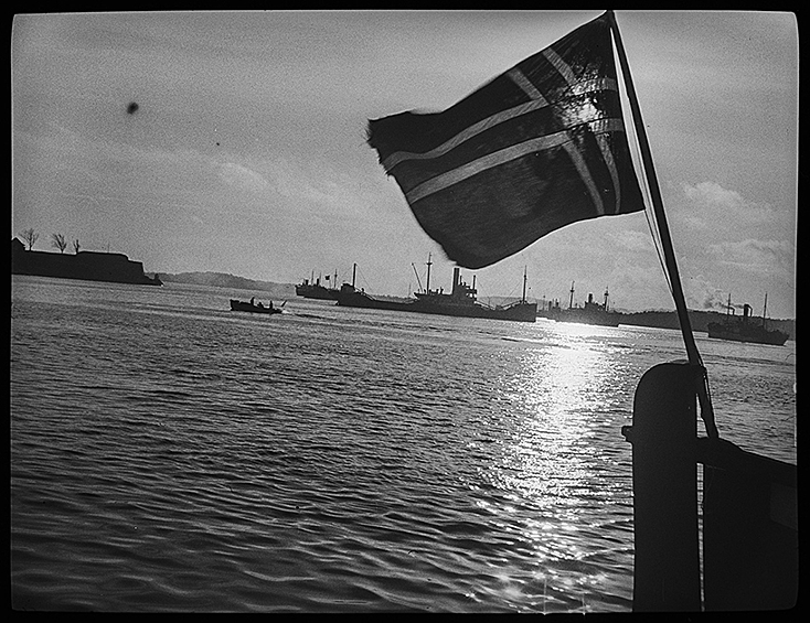 Норвежский флаг на борту судна, на фоне немецких кораблей и патрульного катера. Норвегия, 1940 год
