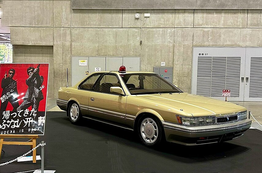 Nissan Leopard (F31) из культового детективного фильма Abunai Deka. На золотистом купе ездит один из главных персонажей, старший офицер полиции Юджи Ошита. У нас эта модель известна мало: угловатое хардтоп-купе было построено на заднеприводной платформе Nissan Laurel C32 и Skyline R31, и выпускалось с 1986 по 1992 год. Комплектовалась эта модель исключительно моторами V6 объёмом 2 или 3 литра, атмосферными и с наддувом. Интересно, что она даже недолго продавалась в США — как Infiniti M30.
