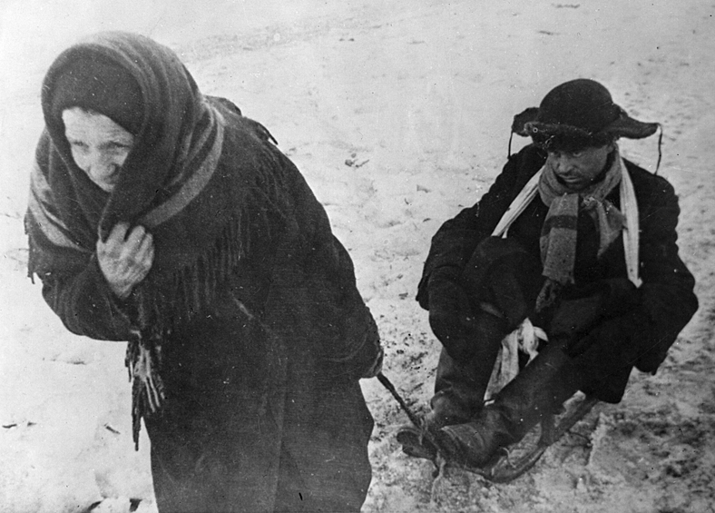 В дни блокады Ленинграда. Жители блокадного Ленинграда: женщина везет ослабевшего от голода мужа на санках, 1942 год