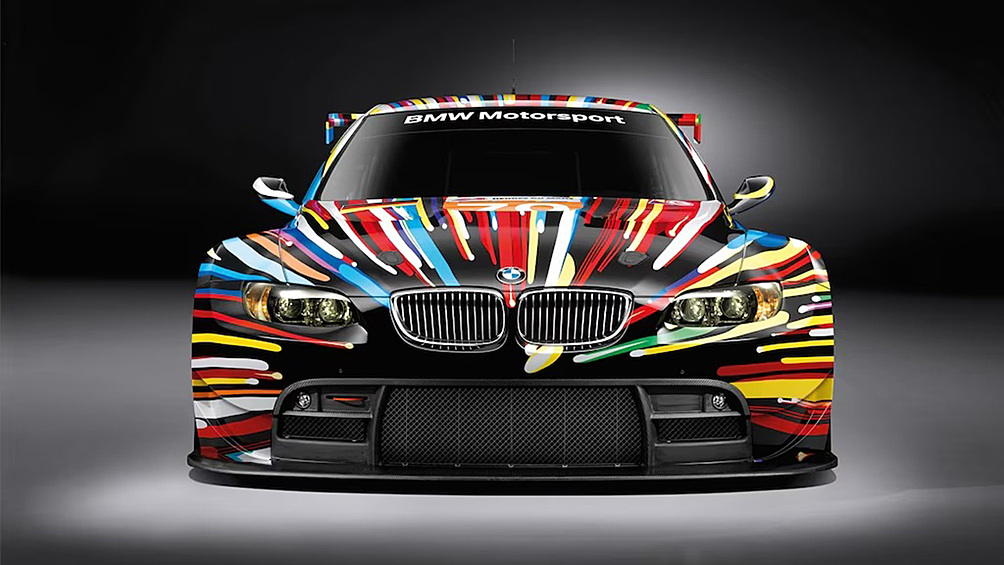 В 2010-м BMW доверяет кузов M3 GT2 Джеффу Кунсу — королю китча и гламура. Его версия? Взрыв цвета, линий и «взрывной» графики, словно машину разорвало в ускорителе частиц.
