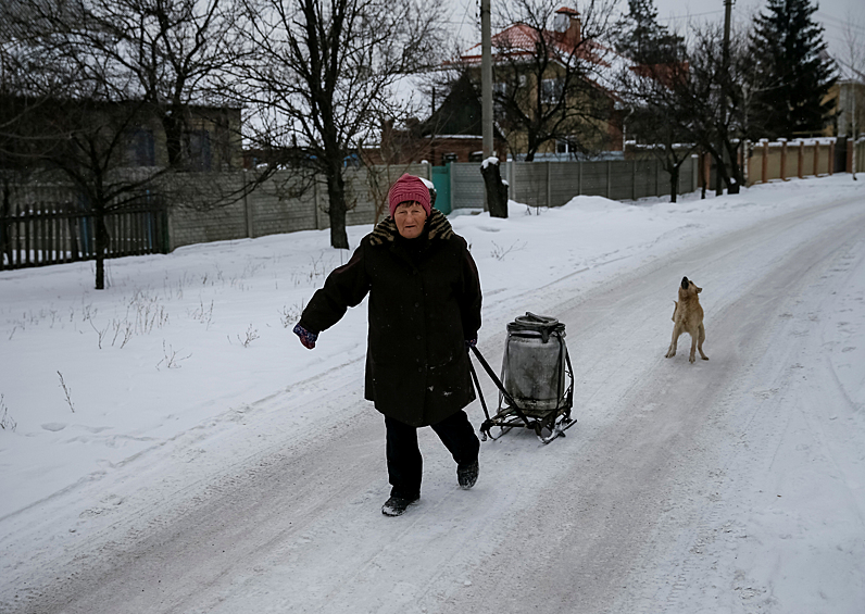 Женщина везет на санках бидон с гуманитарной помощью