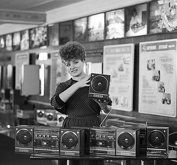 Кассетный магнитофон — мечта молодежи 1980-х. Пригласишь друзей домой, а там такое!.. Круче только видеомагнитофон — его можно и на квартиру обменять (привет сегодняшним ипотечникам). На фото: инженер рекламного отдела Бердского радиозавода показывает новые переносные кассетные магнитолы «Вега-335-стерео». 1987 год