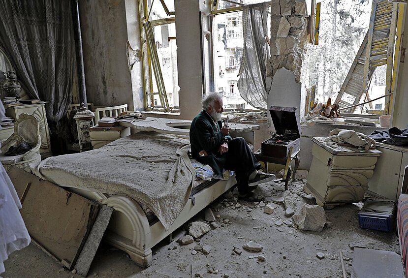 70-летний Мухаммед Мохидэйн Анис курит трубку в своей разрушенной спальне, слушая музыку на своем проигрывателе в районе аль-Шаар в Алеппо