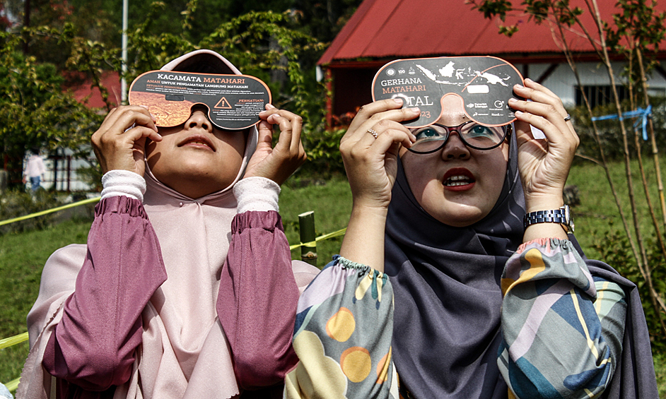 Люди наблюдают гибридное солнечное затмение в Индонезии