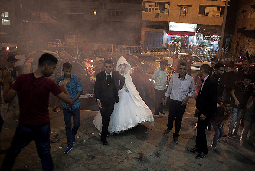 Из серии «Почему Газа?». Молодожены Саед Абу Асер (Saed Abu Aser) и Фаластин (Falasteen) проходят сквозь дым от фейерверков в день бракосочетания. Свадьбы стали редкими радостными событиями, которые могут разбавить мрачное существование в секторе Газа. 