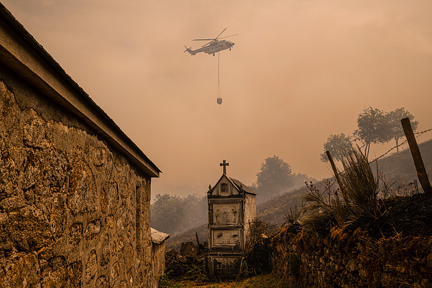 Пожарный вертолет пролетает над городом Вилар, Испания, 12 августа 2025 года