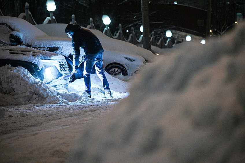 Мужчина расчищает автомобиль от снега в Москве