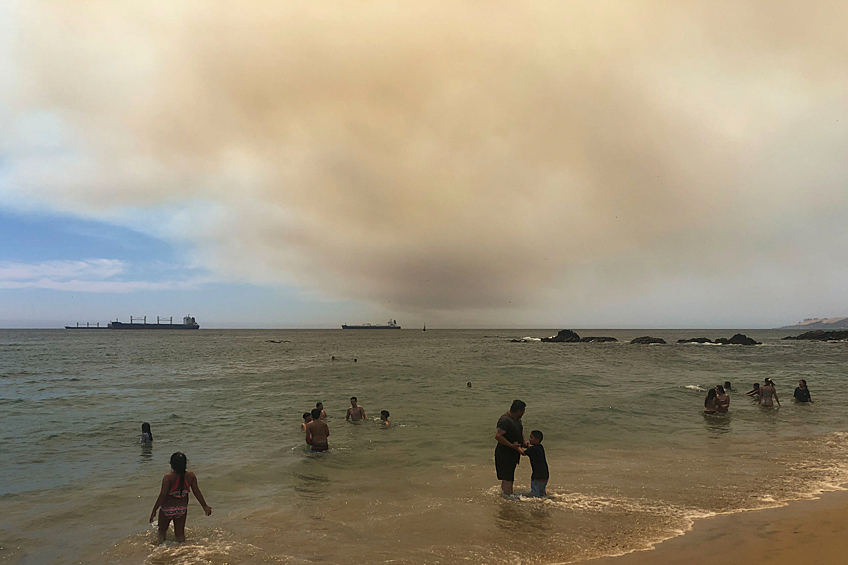 Люди на пляже в Вальпараисо, на фоне лесного пожара в заповеднике озера Пенуэлас