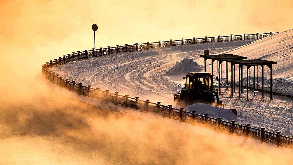 Трактор убирает снег при температуре воздуха около -27 градусов Цельсия на Центральной набережной Енисея в Красноярске